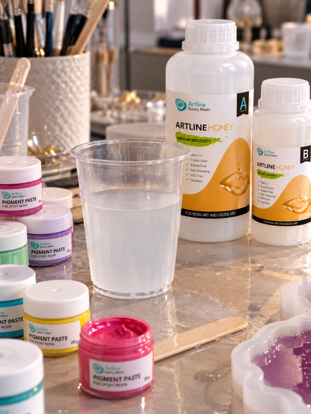 Artline Honey epoxy resin bottles and a cup of cloudy, crystallized resin on a resin art workbench