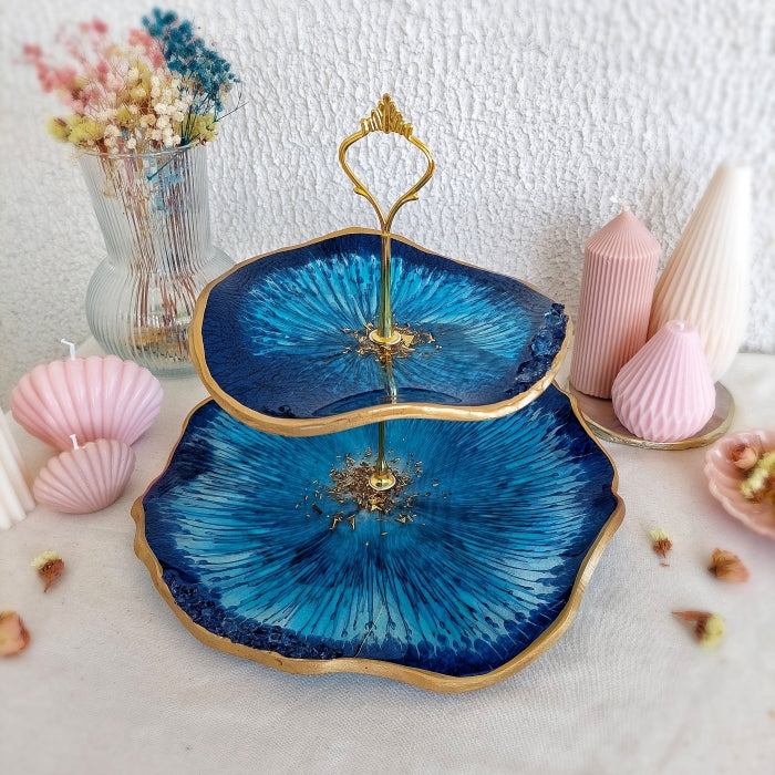 Dark azure resin cake stand created with pigment paste, surrounded by decorative candles and dried flowers.