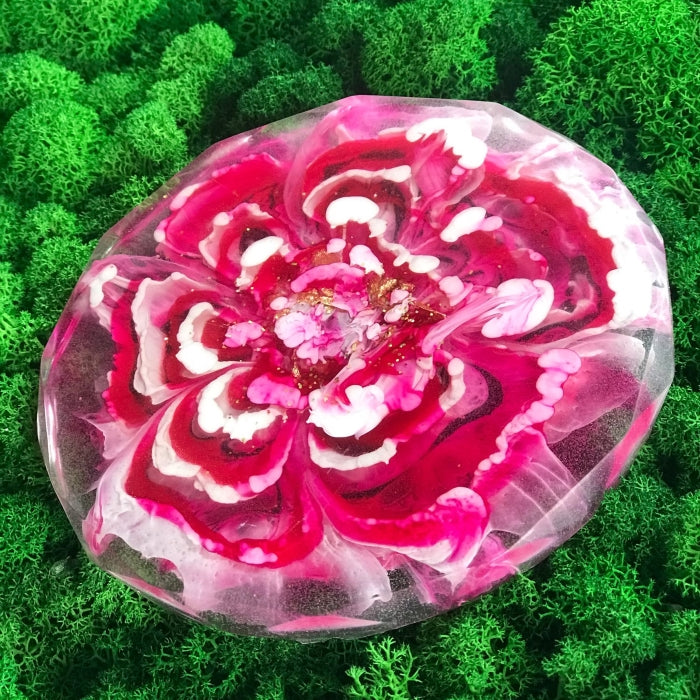 Pink epoxy resin art with intricate flower design on green background.