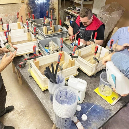 Atelier avec plusieurs pièces finies sur une grande table, alors que des maîtres de l'époxy se préparent à couler de la résine époxy lors d'une masterclass de planches à découper utilisant les résines époxy Artline