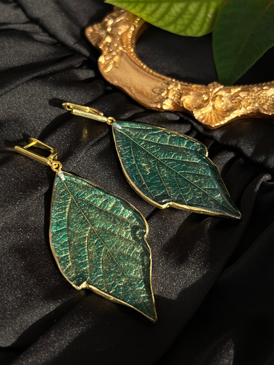 Green leaf-shaped earrings made with crystal epoxy resin on a black textured background.