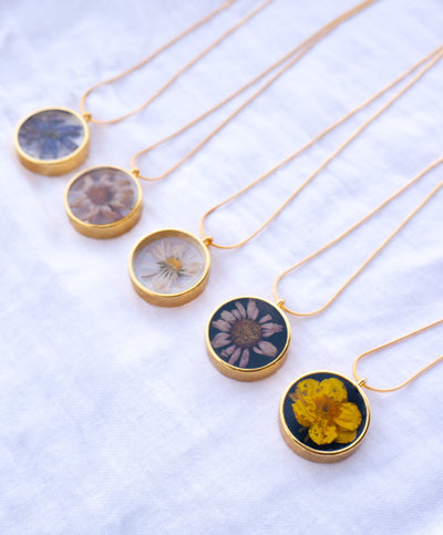 Flower pendants made with crystal epoxy resin on gold chains displayed on a white background.