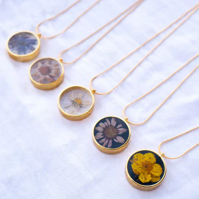 Crystal epoxy resin jewelry pendants with floral designs on gold chains.