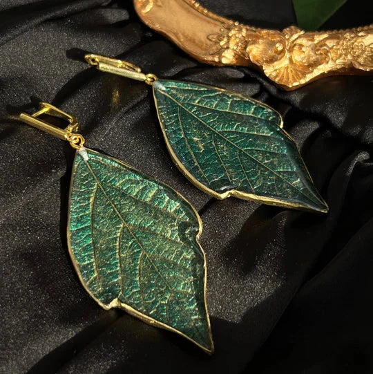 Green leaf-shaped jewelry made from crystal epoxy resin on dark fabric background.